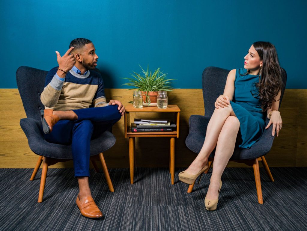 Woman wearing teal dress sitting on chair talking to man