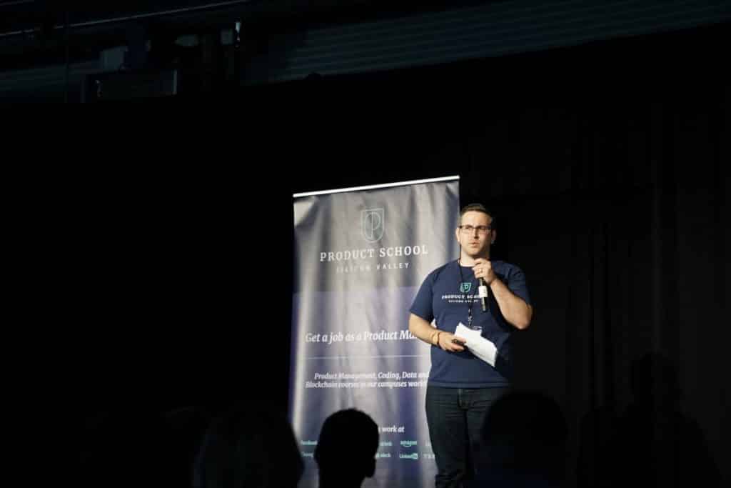 man on stage giving a presentation at a conference with an audience in the foreground