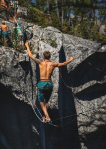 Slackline suspendend from rock face while a shirtless man balances on it